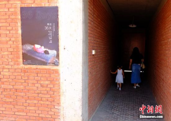 8月12日，位于北京草场地艺术中心举办“裸女睡钢丝床”行为艺术展的某画廊，一名女性参观者带着小孩在紧闭的大门前一探究竟。8月9日，一位女行为艺术家在此举办题为《36天》的展览，她计划裸睡在钢丝床上36天，期间将正常吃饭、睡觉等，引起关注。 中新社发 侯宇 摄