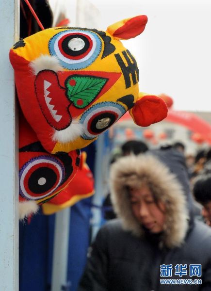  在河南浚县古庙会上，一位游客从一个销售布老虎工艺品的展位前经过。