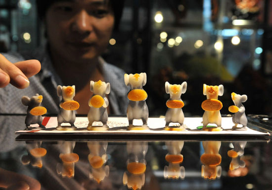 7月10日，一名客商在2014中国昆明泛亚石博览会上展示用玉石雕刻的一组生肖鼠工艺品。资料图