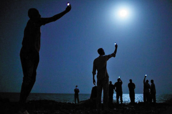 John Stanmeyer，信号。2013年2月26日，吉布提的海岸，一些非洲移民在吉布提的海滩上手举自己的手机，搜寻便宜的手机信号用以联系他们的亲人。对于来自索马里等非洲国家的移民来说，吉布提通常是他们前往欧洲寻求好生活的中转站。