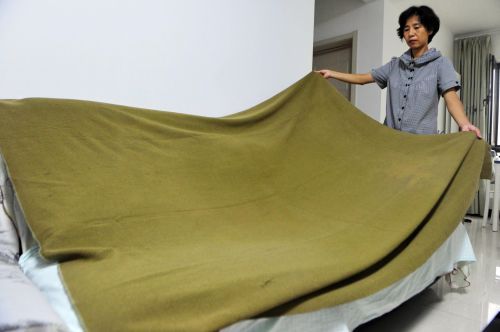  21日，李女士正在展示她父亲保存下来的毛毯。70多年过去了，这床军绿色的毛毯保存良好。本报记者 王媛 摄
