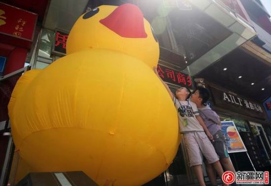 7月10日，在民主路一家商铺前，两名小朋友踮着脚尖摸着这只充气大黄鸭。（记者刘志龙摄）
