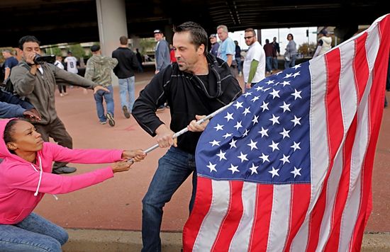 在一场圣路易斯公羊队的橄榄球赛后，弗格森事件的示威者Cheyenne Green紧抓一面美国国旗，以防被一名球迷夺走。2014年10月19日摄于圣路易斯爱德华·琼斯穹顶球场。 《圣路易斯邮报》摄影团队 图