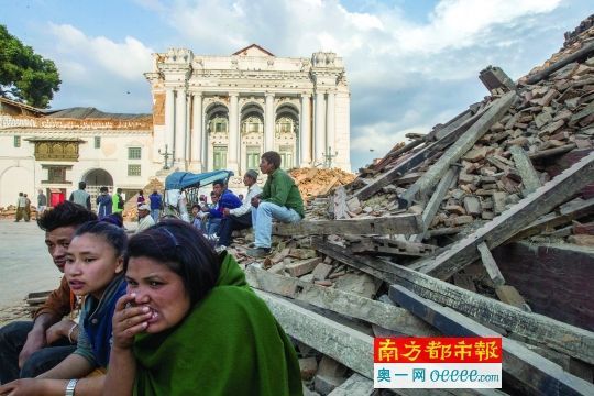 昨日傍晚，加德满都杜巴广场，当地居民和游客坐在倒塌的古迹废墟旁，他们身后是受损严重的加德满都老皇宫。 谭庆驹 摄