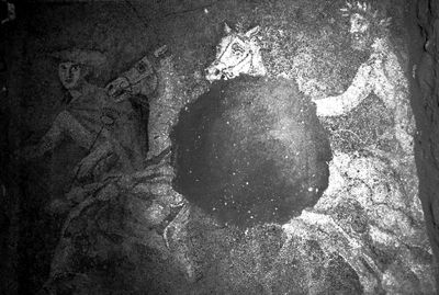 古墓中发现的马赛克地板。画面中，头戴桂冠的长髯男子驾驶着双匹白马战车，古希腊神话中众神之信使赫耳墨斯在马车前牵引。