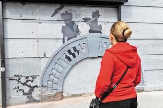 一名女子19日在纽约布鲁克林区一栋大楼墙面前，欣赏班克斯的涂鸦作品。这面墙的建筑物业主把该涂鸦作品视同宝物。