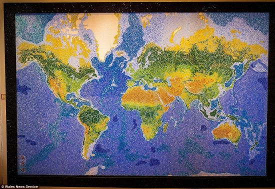 他用镊子将玻璃颗粒粘到有机玻璃板上，拼画出陆地、国家、城市、河流等。