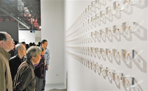 市民正在观看一件名为《DNA》的作品。该作品在墙上贴满了透明的小立方块,每个里面都有一团咀嚼过的造型不同的口香糖。 记者 熊明 摄