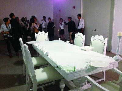 黎薇的装置作品《我很平静》。一张白色餐桌边缘摆放了一些易碎或锋利的日常用品，摇摇欲坠。