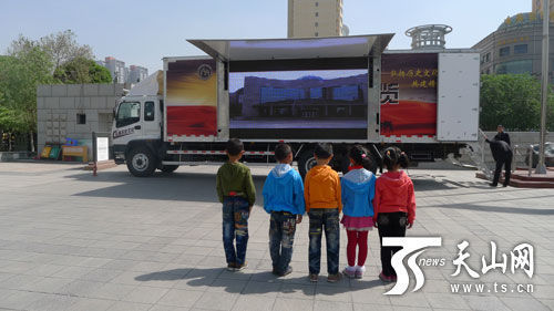 几位儿童正在观看流动博物馆展览车侧面的LED显示屏上播放的节目 