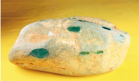 翡翠原石 22cm×15cm×9cm 5.263KG  　　此块国宝级翡翠原石，为藏家蒋先生于1989年从中缅边境缅甸老农手中发现。薄薄的表皮难掩呼之欲出的翠绿，四周开了13个天窗均透出翡翠的优质色泽，在强光下通体透明。经国家珠