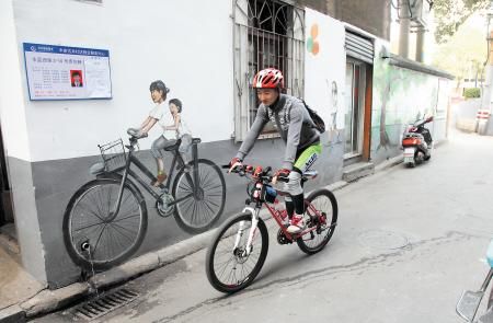 一个自行车爱好者骑过小巷，与墙上怀旧的骑车插画相映成趣。