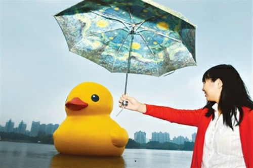 一位女游客在细雨中为大黄鸭“撑伞”。袁婧 摄影报道