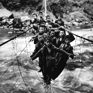 《独龙族放学的小孩》 　独龙族地区交通之艰险是罕见的，要过江就只有走藤篾桥。这种桥是以四根藤绳横跨江面，铺上四根细竹。人在上面行走， 摇晃很大，使人感到头晕目眩。