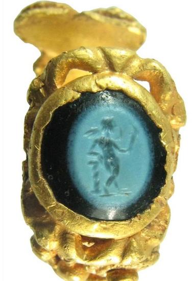 该纯金指环镶嵌着黑色玛瑙和绿色宝石，绿色宝石上还镶刻着一个爱神丘比特的裸体形象。