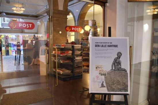 这是8月23日在丹麦邮政局门口拍摄的小美人鱼雕像百年诞辰纪念邮品招贴画。